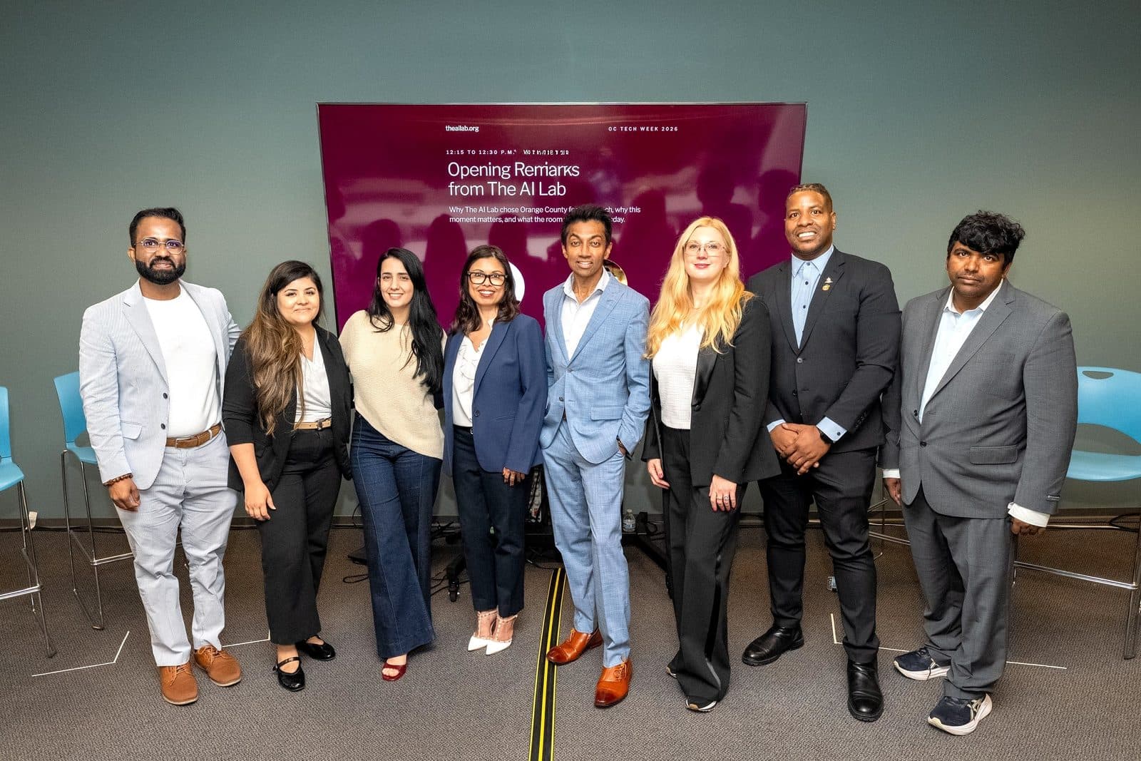 Eight people from The AI Lab team and its partners stand together in front of a screen reading Opening Remarks from The AI Lab, OC Tech Week 2026.