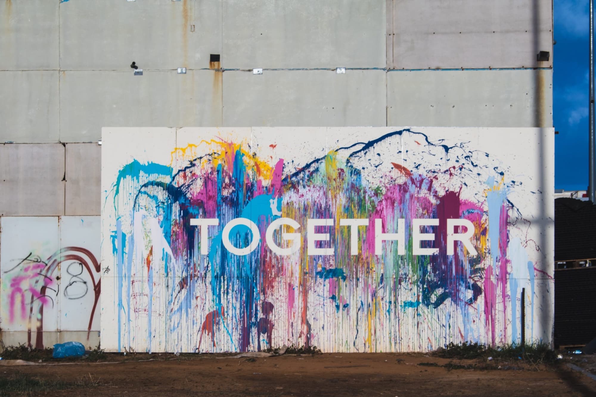 A graffiti mural reading "Together" in white block letters over a wall of cascading multicolour paint. The image accompanies Joshua D. Baron's essay "Trust Cannot Be Engineered Behind Closed Doors" on LinkedIn.